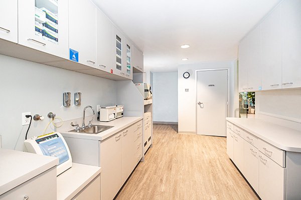 A clean, modern medical laboratory at South Redondo Dental features white cabinets, countertops, and drawers, a sink, medical equipment, and wood-style flooring under bright overhead lighting. The door at the end is labeled “LABORATORY.”.