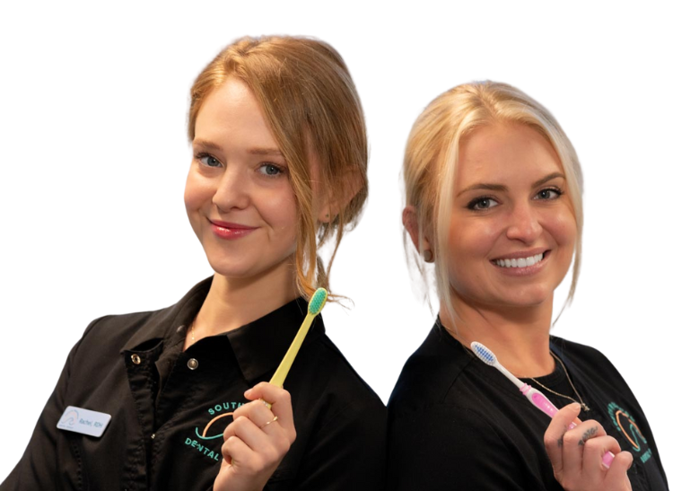 Two women wearing black dental uniforms smile while holding toothbrushes, ready for teeth cleaning. One has a name tag, and both stand back-to-back against a plain light background.